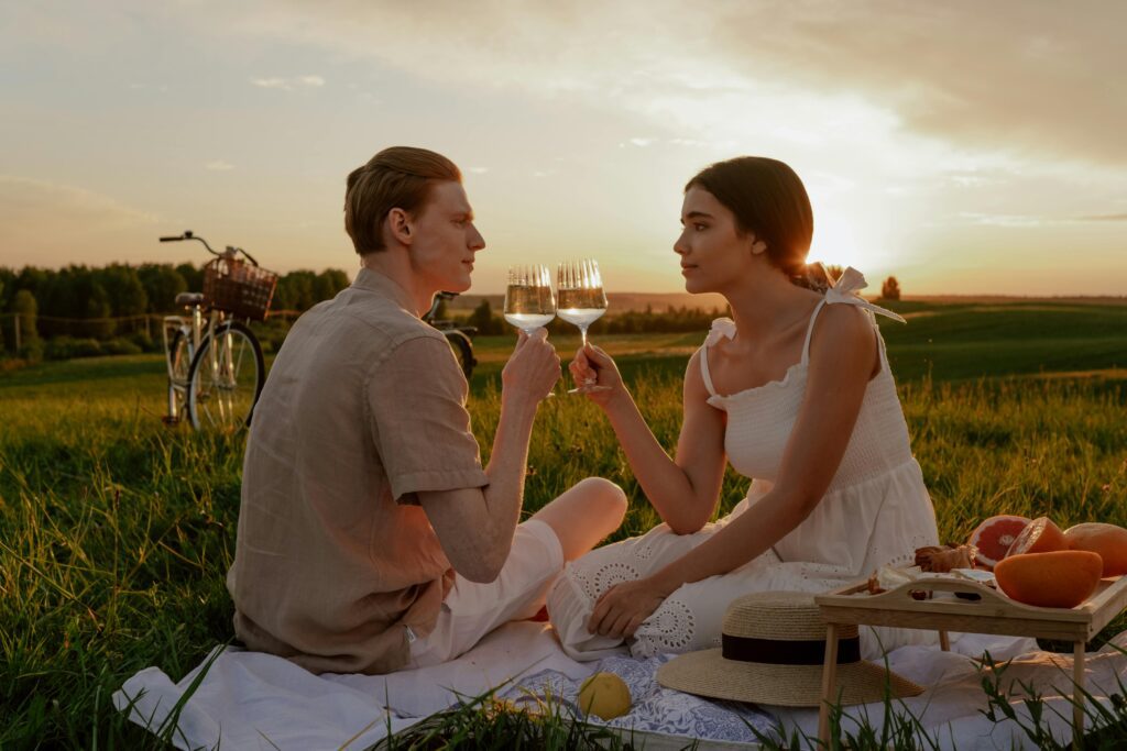Couple enjoying a romantic picnic with wine at sunset in a serene outdoor setting.